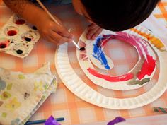 This may contain: a child painting on paper plates with paintbrushes and other crafting supplies nearby