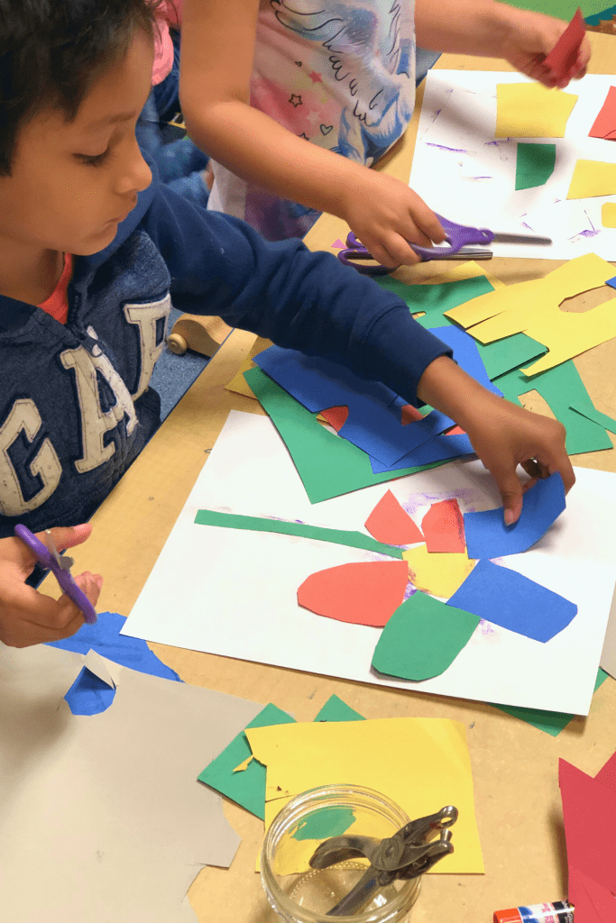 A child glues a petal shaped piece of blue paper to his eric carle inspired collage flower.