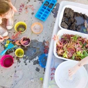 Overhead view of a DIY mud kitchen with dirt, water, and leaves. Two children are present but just off frame.