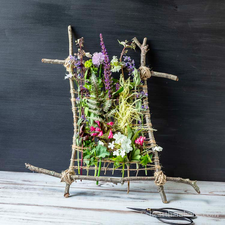 sticks tied in a square. flowers are woven on to them.