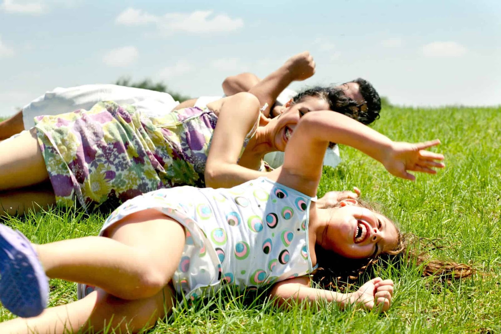 family enjoying the outdoors rolling down a grassy hill