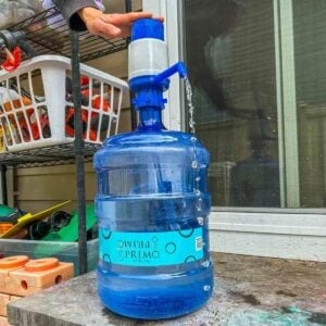 A person pushes on the top of a hand pump getting water from a water jug