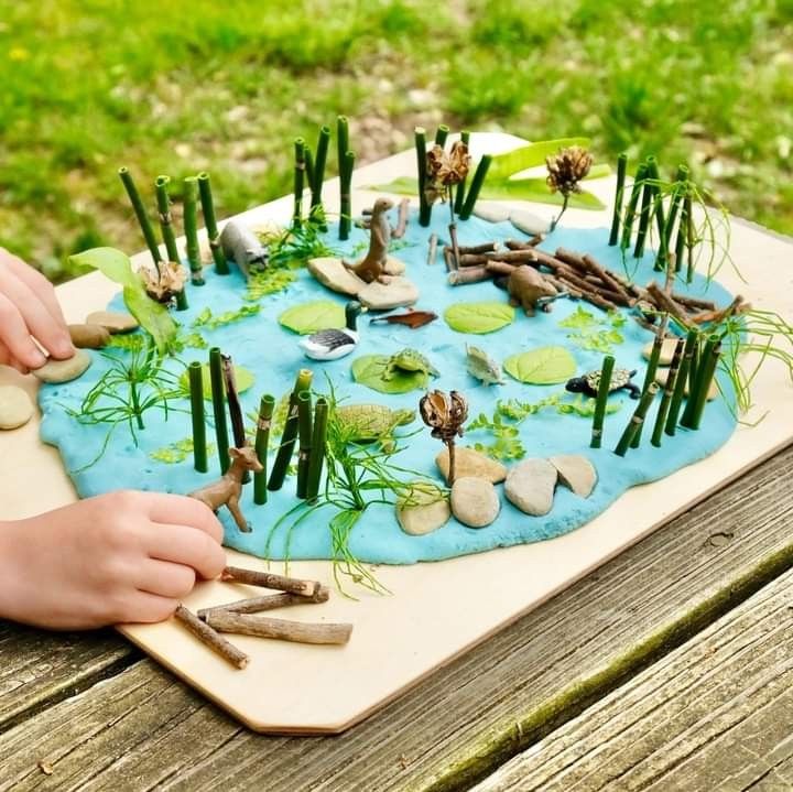 This may contain: a child's hands are playing with plants and rocks on a table in the grass