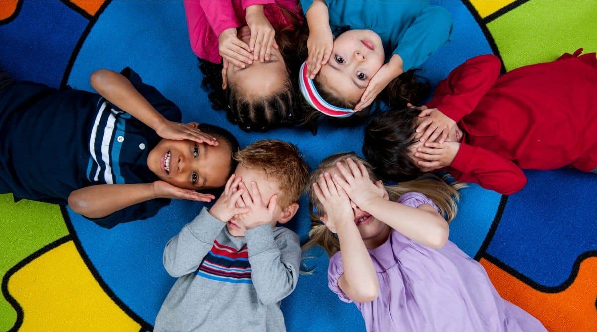 group of preschoolers laying on their backs on a colorful floor playing peek a boo