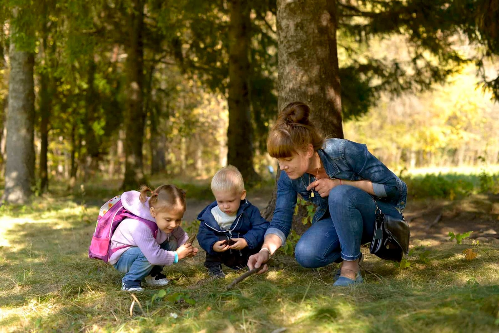 mother, son and daughter out on a nature walk. They are bent down exploring something in the grass